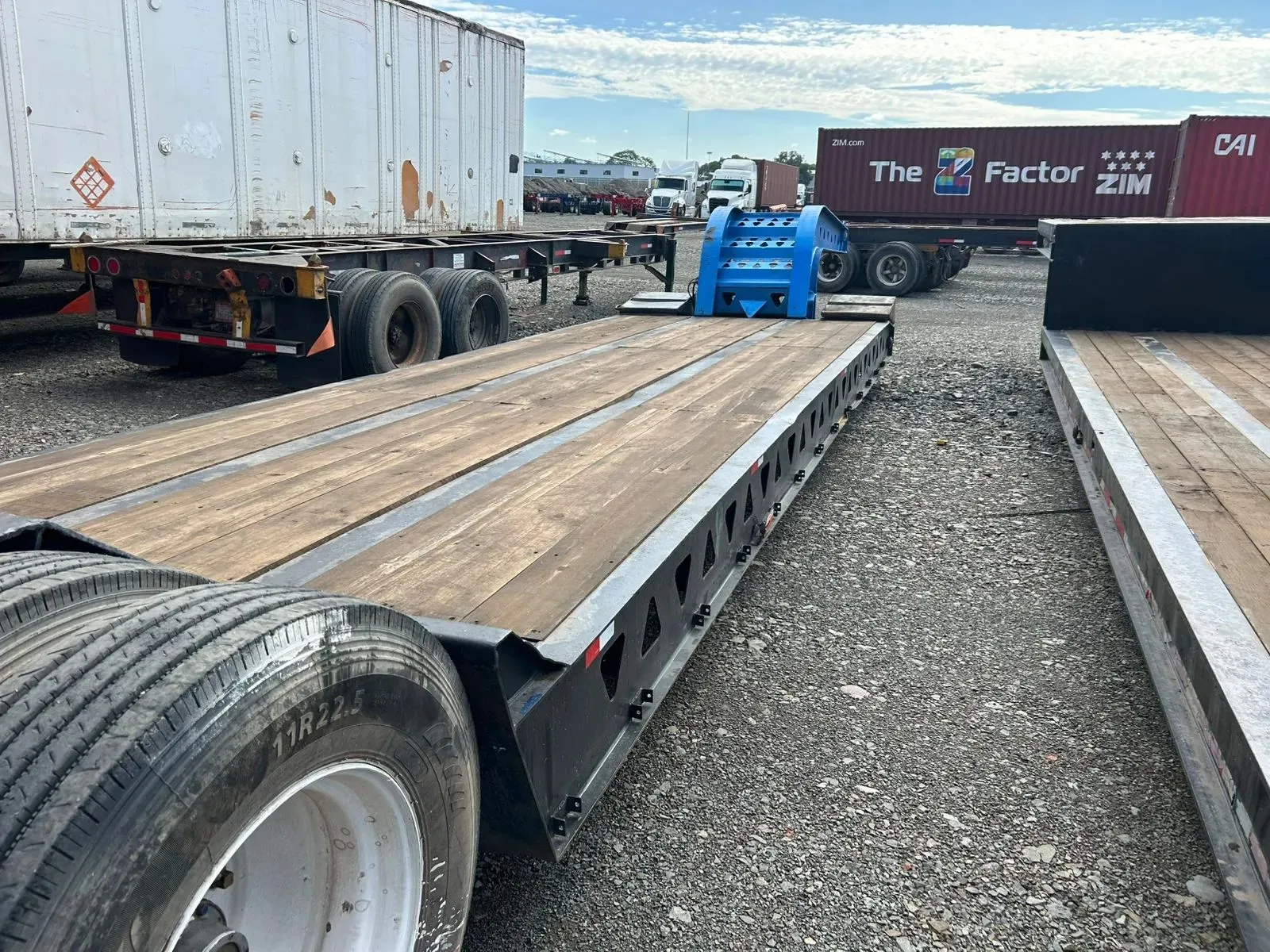 Cama baja con piso de madera y cuello azul, estacionada en un patio de contenedores.