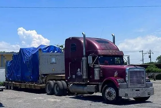 Tractocamión guinda con lowboy y carga cubierta con lona azul.